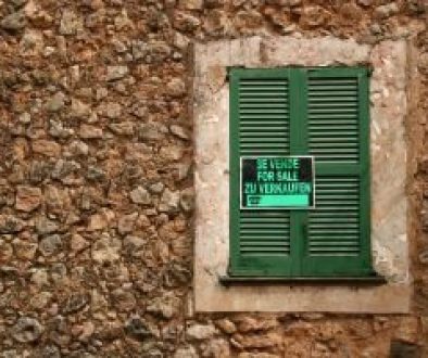 Stone building with green shutters and For Sale sign